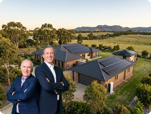 Allan Border and Glenn McGrath standing in front of a rural Victorian property with rooftop solar panels surrounded by open countryside.